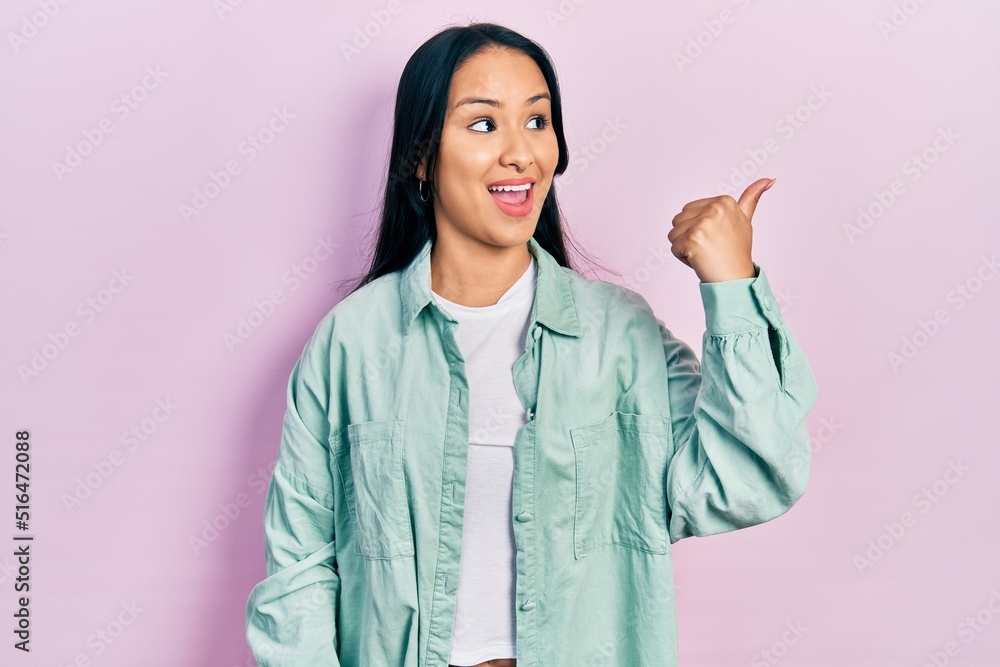 Wall mural Beautiful hispanic woman with nose piercing wearing casual green jacket pointing thumb up to the side smiling happy with open mouth