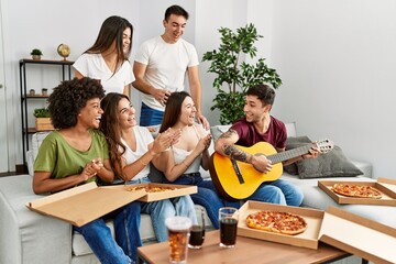 Group of young friends having party eating italian pizza and playing classical guitar at home.