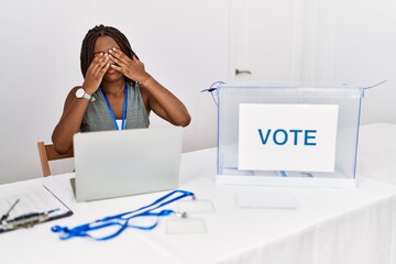 Young african american woman working at political election sitting by ballot rubbing eyes for...