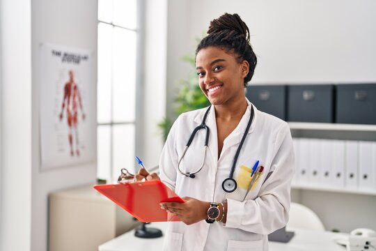 African american woman wearing doctor uniform writing on document at clinic