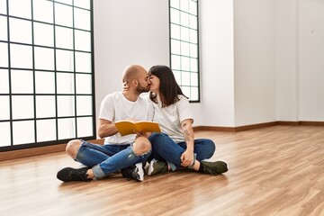 Young hispanic couple kissing and reading book at empty new home.