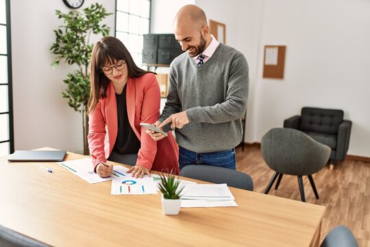Two hispanic business workers smiling happy working using smartphone at the office.