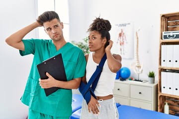 Physiotherapist working with patient wearing arm on sling at rehabilitation clinic confuse and...