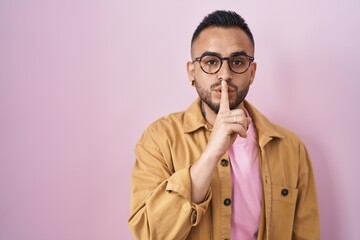 Young hispanic man standing over pink background asking to be quiet with finger on lips. silence and secret concept.