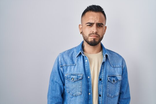 Young hispanic man standing over isolated background skeptic and nervous, frowning upset because of problem. negative person.