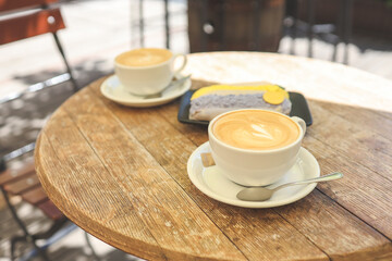 Two cups of coffee and an eclair on a wooden background
