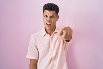 Young hispanic man standing over pink background pointing displeased and frustrated to the camera, angry and furious with you