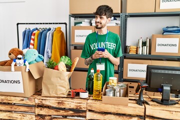 Young hispanic man wearing volunteer uniform usong smartphone at charity center.