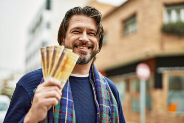 Middle age handsome man holding norwegian krone banknotes at the town
