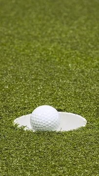 Stop motion of golf ball circling hole.  Vertical video.