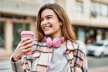 Young blonde woman wearing headphones holding coffee at street