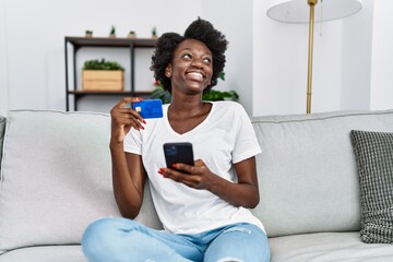 Young african american woman paying using smartphone and credit card at home