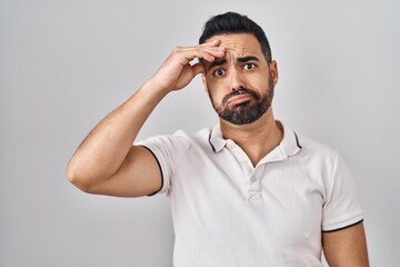 Fototapeta na wymiar Young hispanic man with beard wearing casual clothes over white background worried and stressed about a problem with hand on forehead, nervous and anxious for crisis