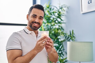 Young hispanic man smiling confident smelling candle at home