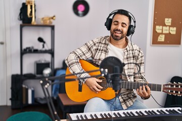 Fototapeta na wymiar Young hispanic man artist singing song playing guitar at music studio