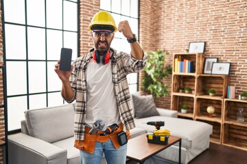 Young hispanic man with beard working at home renovation holding smartphone annoyed and frustrated...