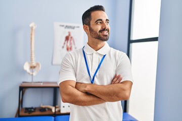 Young hispanic man physiotherapist standing with arms crossed gesture at rehab clinic