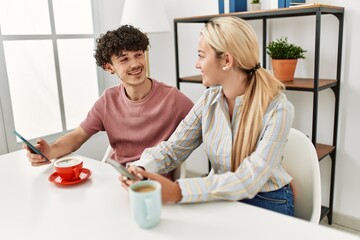 Young couple using smartphone and drinking coffee at home.