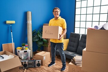 Senior man moving to a new home holding cardboard box angry and mad screaming frustrated and furious, shouting with anger. rage and aggressive concept.