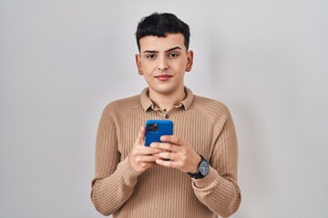 Non binary person using smartphone typing message relaxed with serious expression on face. simple and natural looking at the camera.
