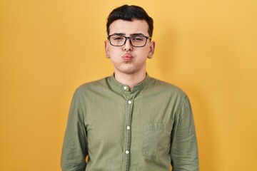 Non binary person standing over yellow background puffing cheeks with funny face. mouth inflated with air, crazy expression.