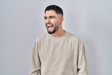 Young handsome man standing over isolated background angry and mad screaming frustrated and furious, shouting with anger. rage and aggressive concept.