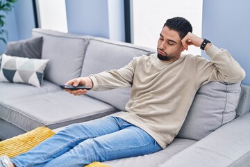 Fototapeta premium Young arab man watching tv with boring expression at home