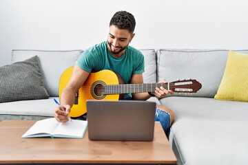 Young arab man composing song using laptop and classical guitar at home