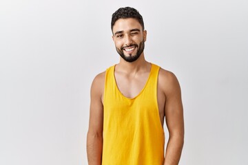 Young handsome man with beard standing over isolated background winking looking at the camera with...