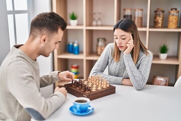 Man and woman couple playing chess sitting on table at home