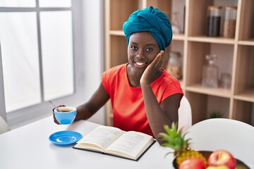 Young african american woman drinking coffee reading book at home