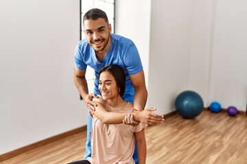 Fototapeta na wymiar Latin man and woman wearing physiotherapist uniform having rehab session using fit ball at rehab center