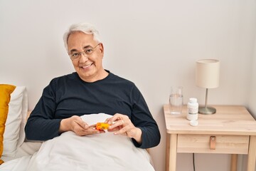 Senior man taking pills treatment sitting on bed at bedroom