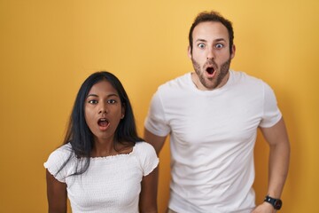 Interracial couple standing over yellow background afraid and shocked with surprise and amazed expression, fear and excited face.