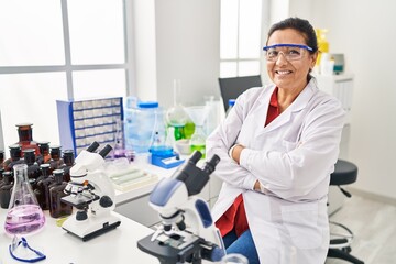 Middle age hispanic woman wearing scientist uniform with arms crossed gesture at laboratory