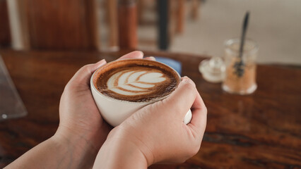 woman hand holding Cappuccino coffee in a beautiful glass on the table favorite cup of coffee concept.