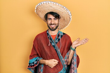 Young hispanic man holding mexican hat smiling cheerful presenting and pointing with palm of hand looking at the camera.