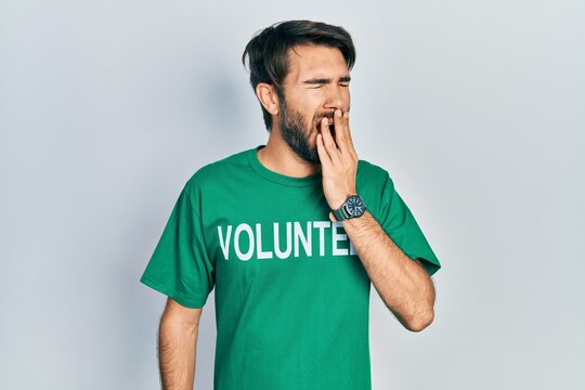 Young hispanic man wearing volunteer t shirt bored yawning tired covering mouth with hand. restless and sleepiness.