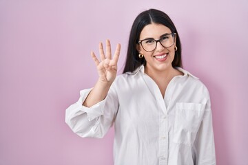 Young brunette woman standing over pink background showing and pointing up with fingers number four while smiling confident and happy.