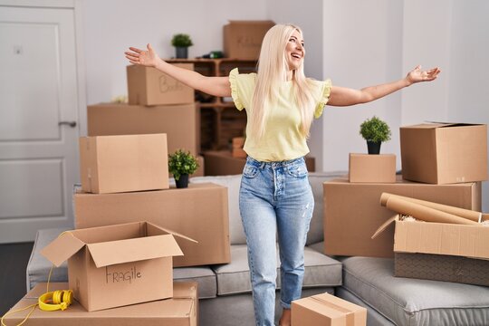 Young blonde woman standing with open arms at new home