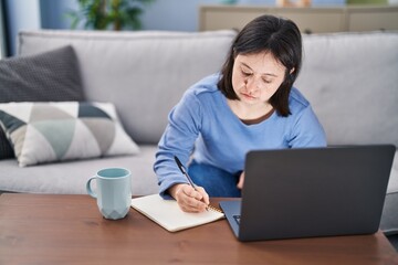 Naklejka premium Young woman with down syndrome sitting on sofa write on notebook studying at home