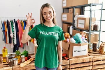 Asian young woman wearing volunteer t shirt at donations stand smiling positive doing ok sign with hand and fingers. successful expression.