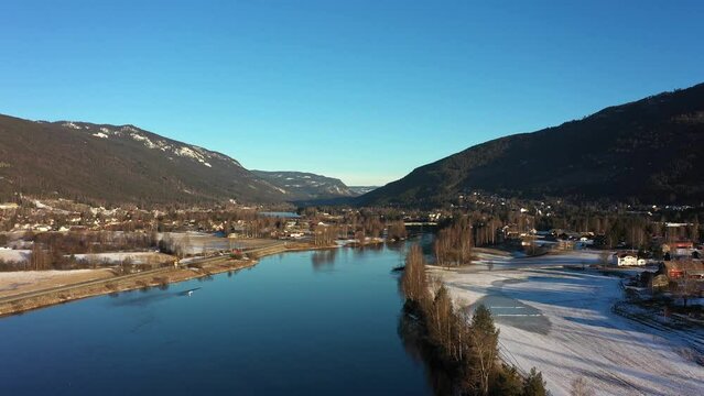 Ascending aerial from Hallingdalselve river to full panoramic view of Nesbyen town during winter morning sunrise - Norway