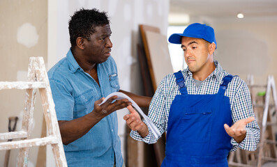 Disappointed african-american man owner of apartment talking to caucasian man repairer about...