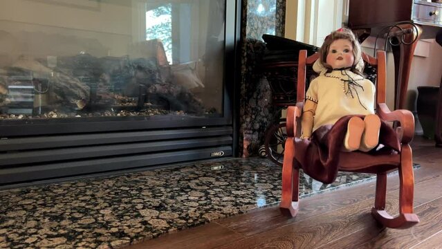 An old and very strange doll sits in a rocking chair against the background of a fireplace, it sways very scary, as if in a horror movie, as if something should happen or has already happened.