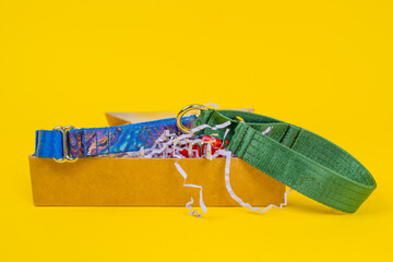 Colorful fabric collars for pets in an open cardboard box, front view, yellow background, copy...