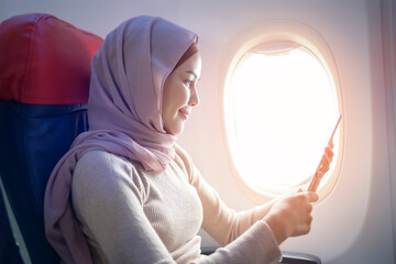 Young muslim woman wearing hijab using smartphone onboard, travel and holidays concept
