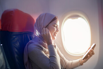 Young muslim woman wearing hijab using smartphone onboard, travel and holidays concept