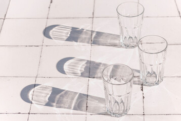 Fototapeta na wymiar glass and sharp shadows stands on a white tiled table. top view of glass
