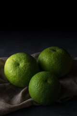 freshly harvested green skin oranges, also called seville, high vitamin C citrus fruit with water droplets on rustic dark background  with space for text